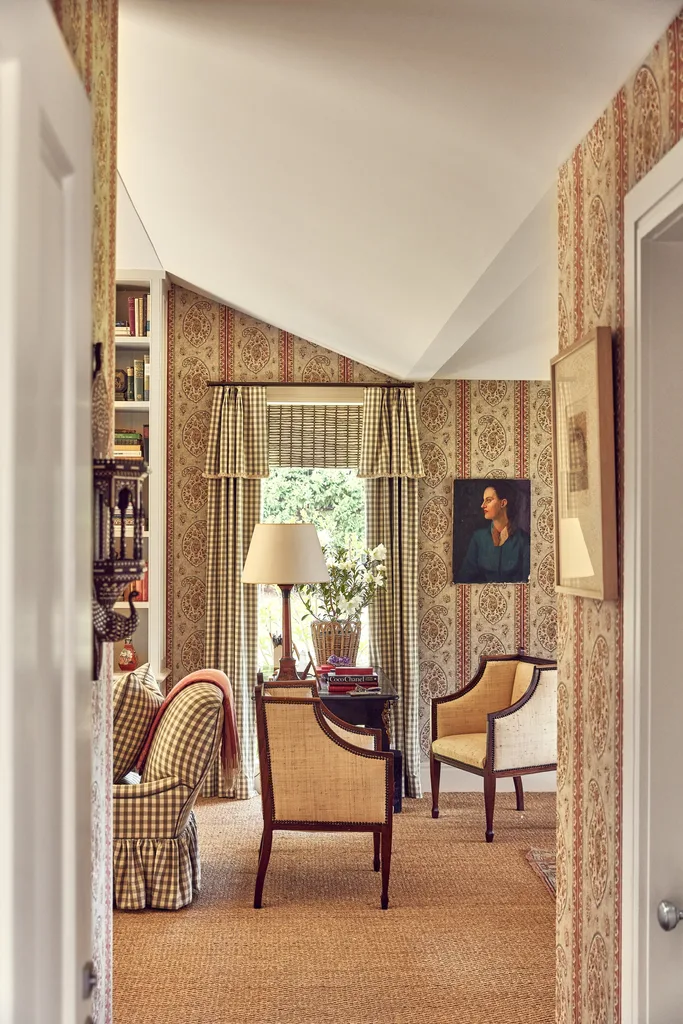 The view of a study from the hallway, walls are covered in paisley wallpaper, timber desk has a lamp atop it