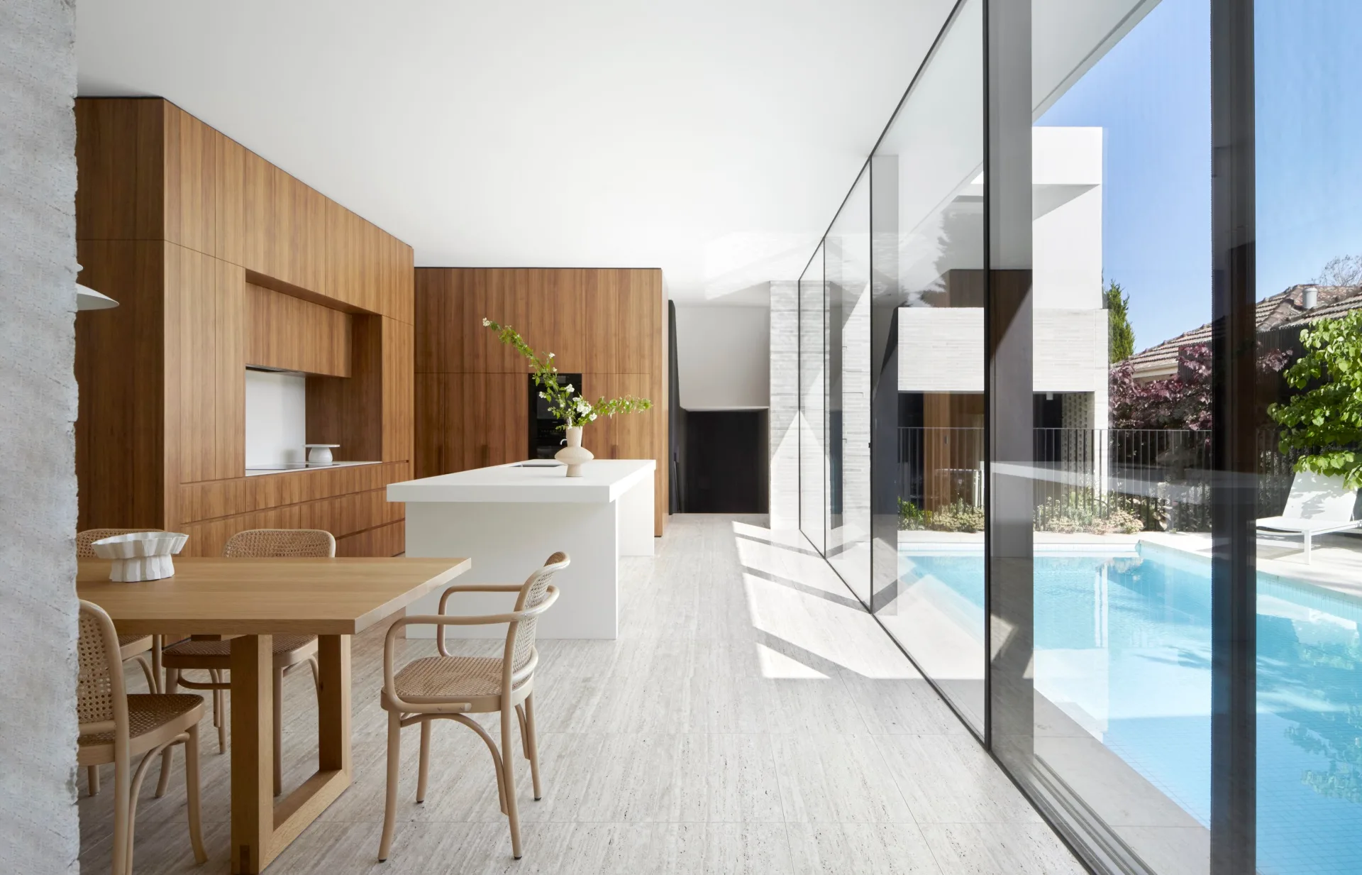 An open-plan kitchen and dining area with floor-to-ceiling windows looking out to a swimming pool