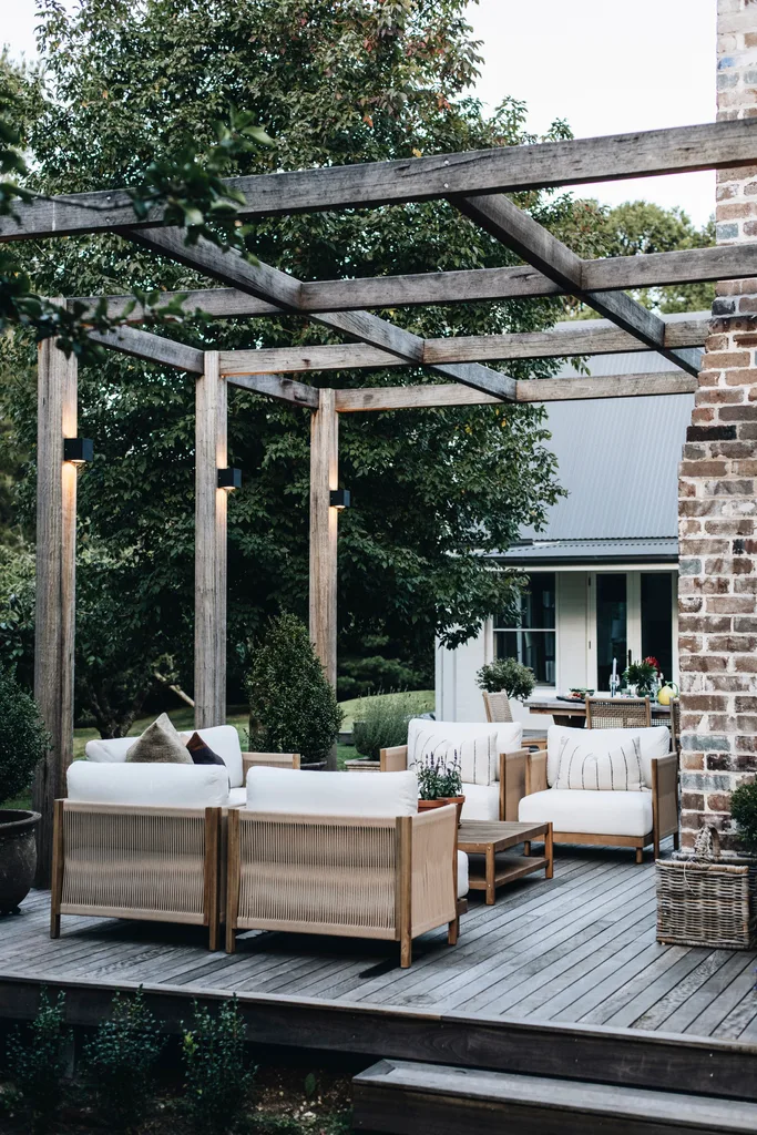 Outdoor decking area beneath a pergola with white armchairs