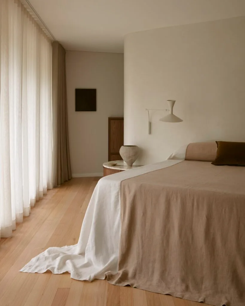 Linen draped over a large bed in a contemporary, beige-hued bedroom