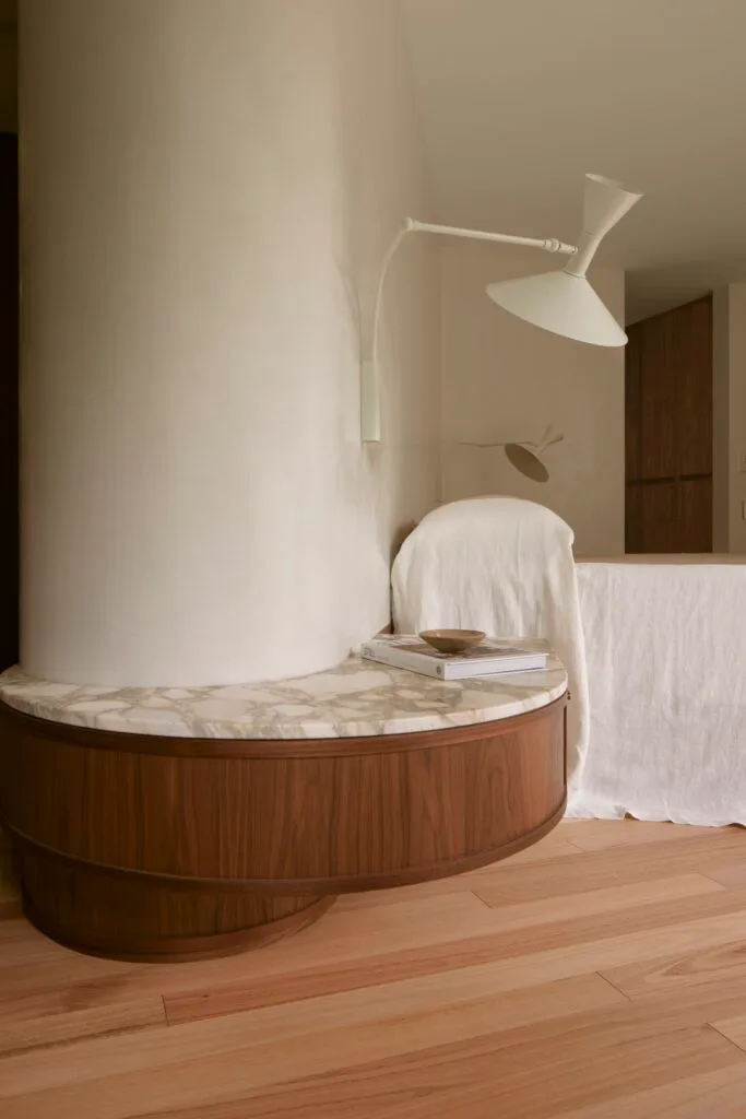 Curved timber cabinetry topped with marble in a neutral-toned bedroom