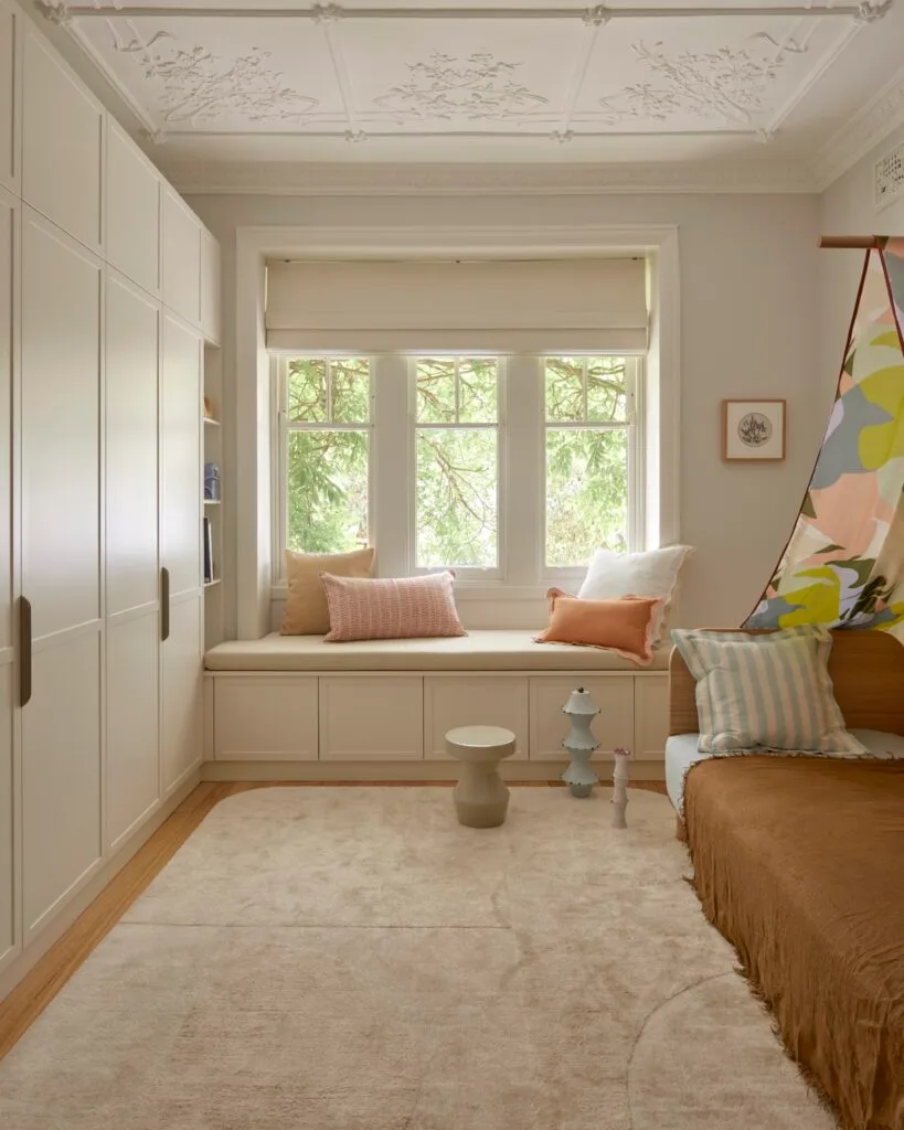 A kid's bedroom with a window seat and beige rug