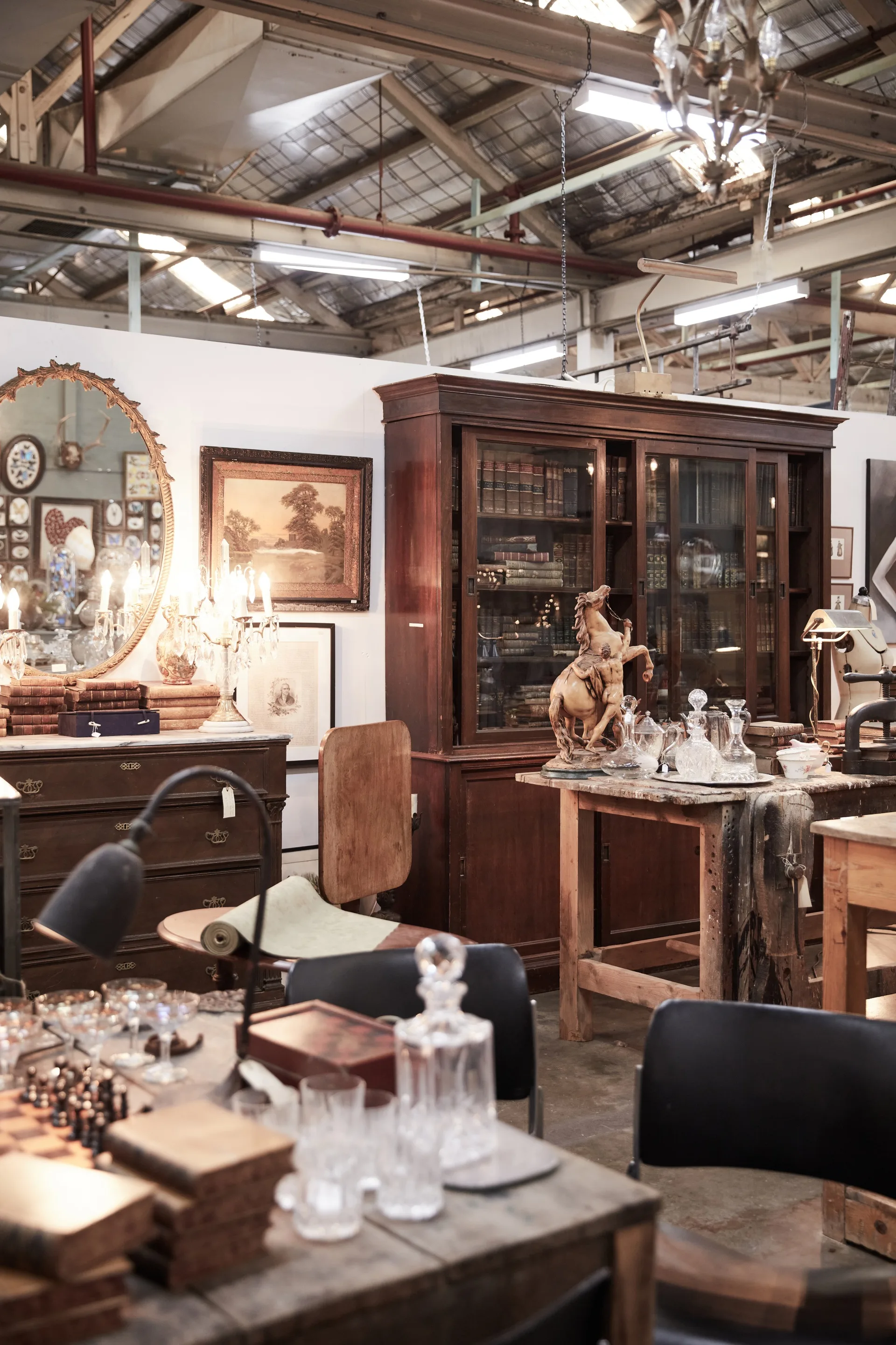 A warehouse filled with antique furniture including a timber cabinet, marble horse sculpture, gilt mirror and chessboard