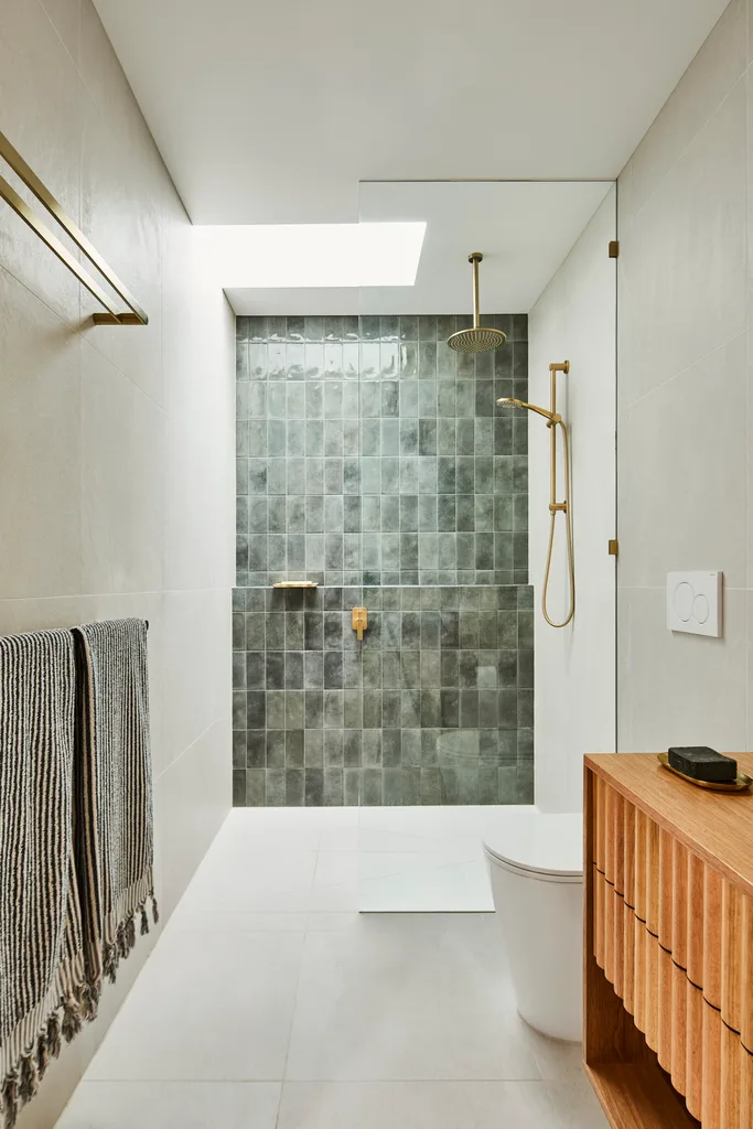 a bathroom with a green tiled shower and skylight