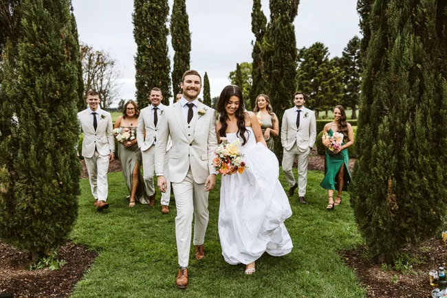 Lucy and Jack with the wedding party walking behind them through trees
