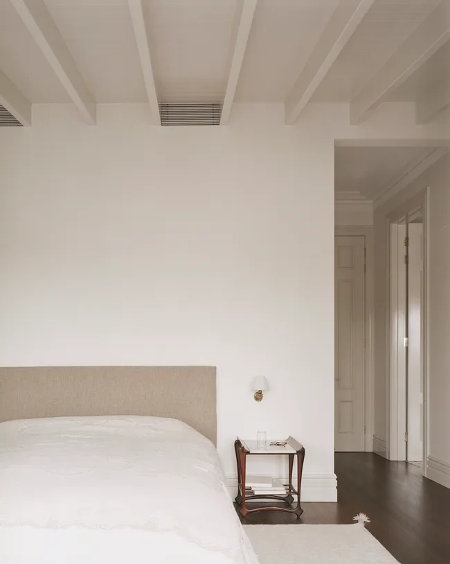 A neutral toned bedroom with white walls, white bedding and a small bedside table