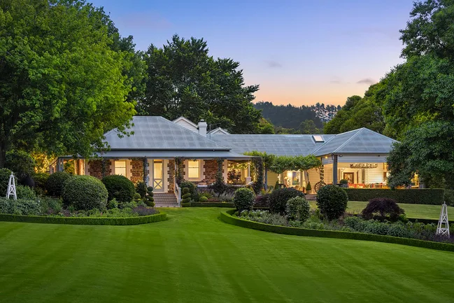 A country home with lush green grass and lights on inside at dusk