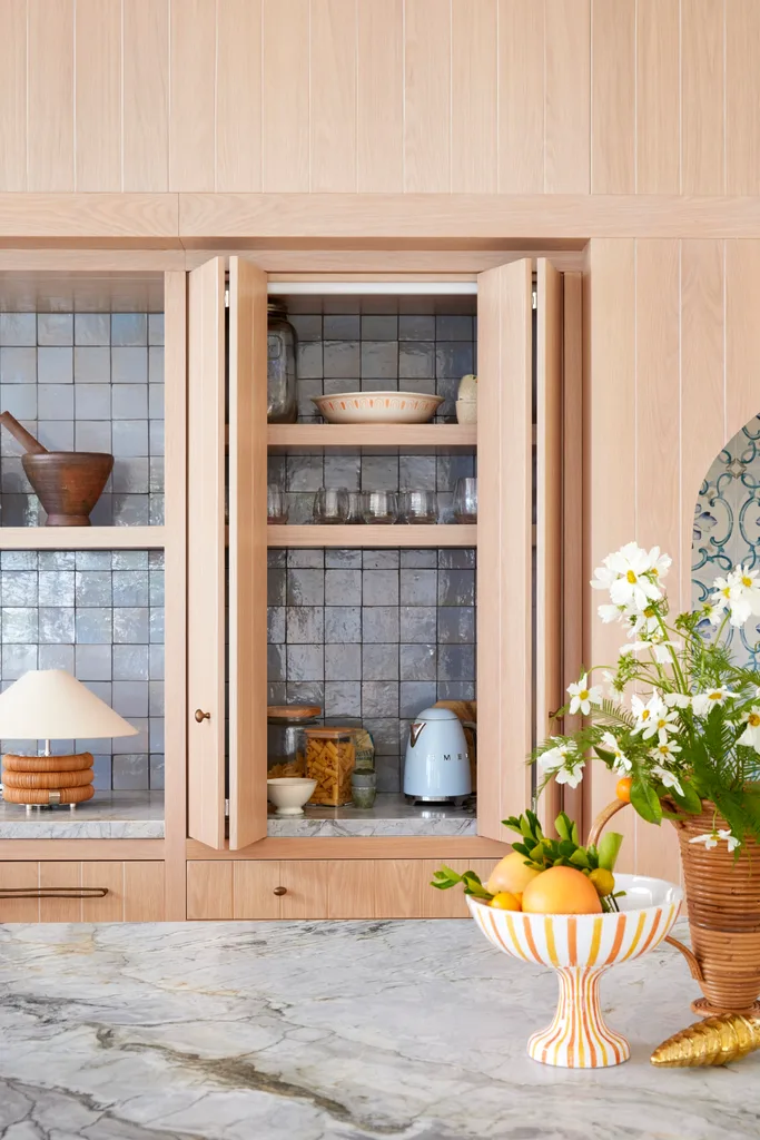 Oranges in a bowl on a marble kitchen bench with open cabinets exposing glassware and a Smeg kettle