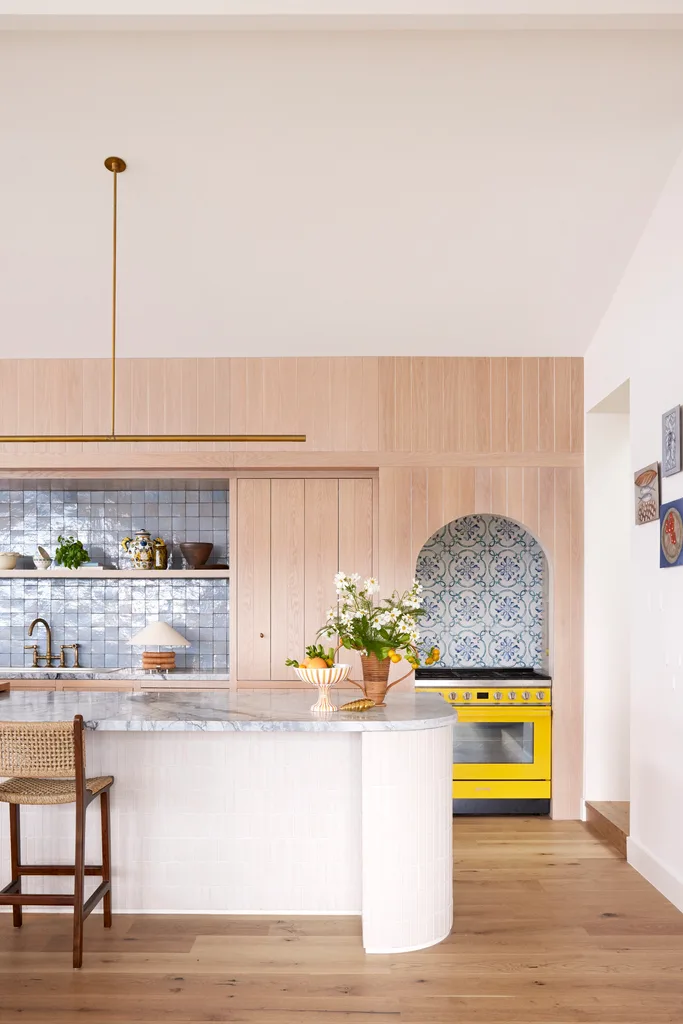 A bright kitchen with timber and marble accents and a stand-out yellow oven