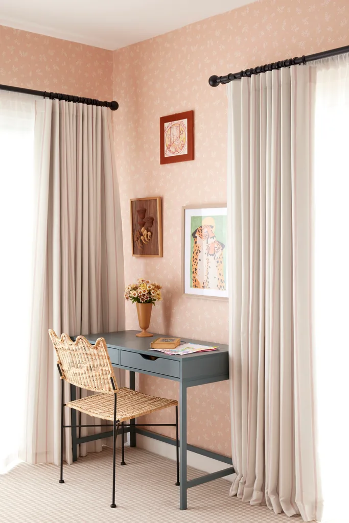 A teal coloured desk with a rattan chair and framed prints hanging on a pink wallpapered wall