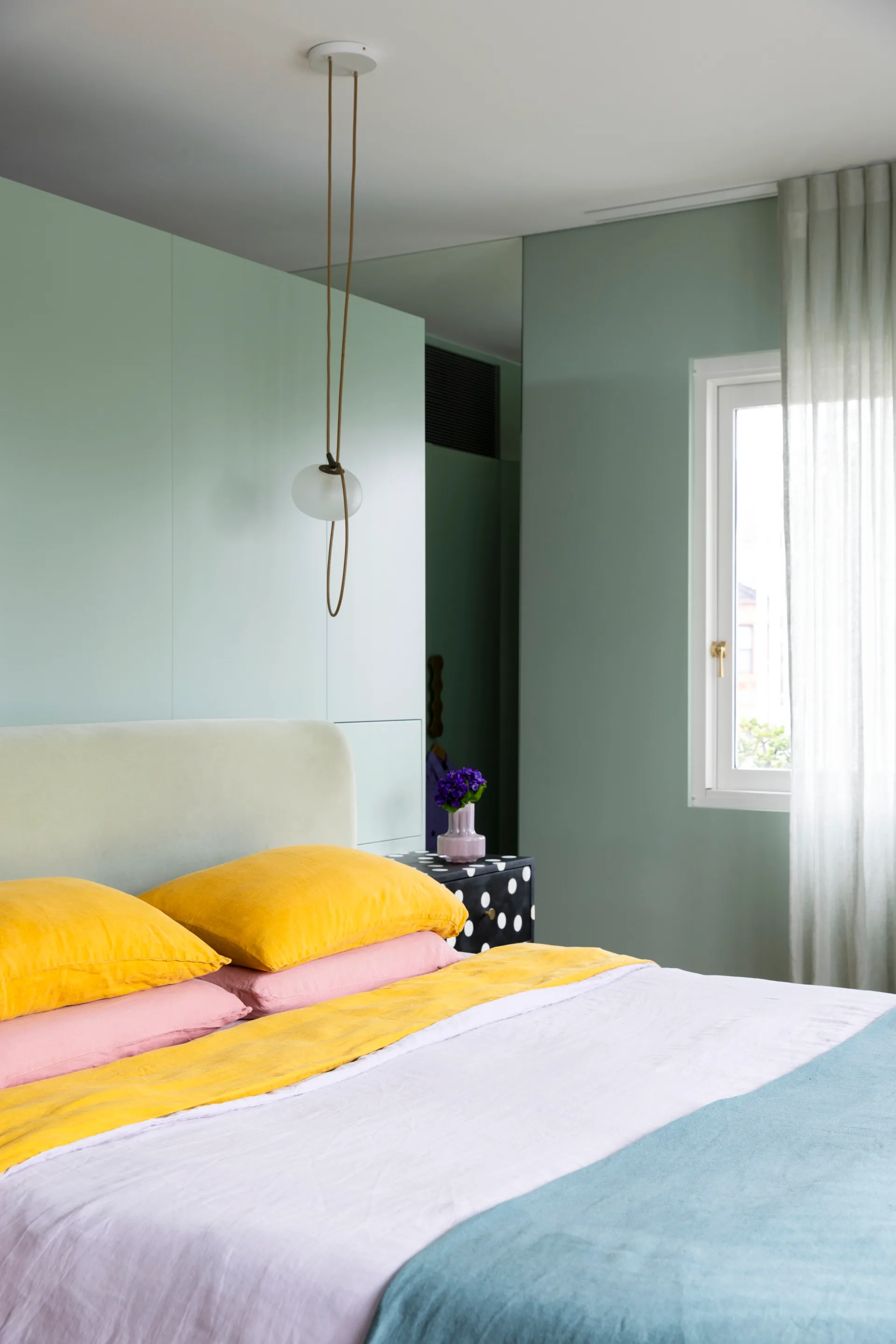 A sage green bedroom with a pendant light and bright bedding