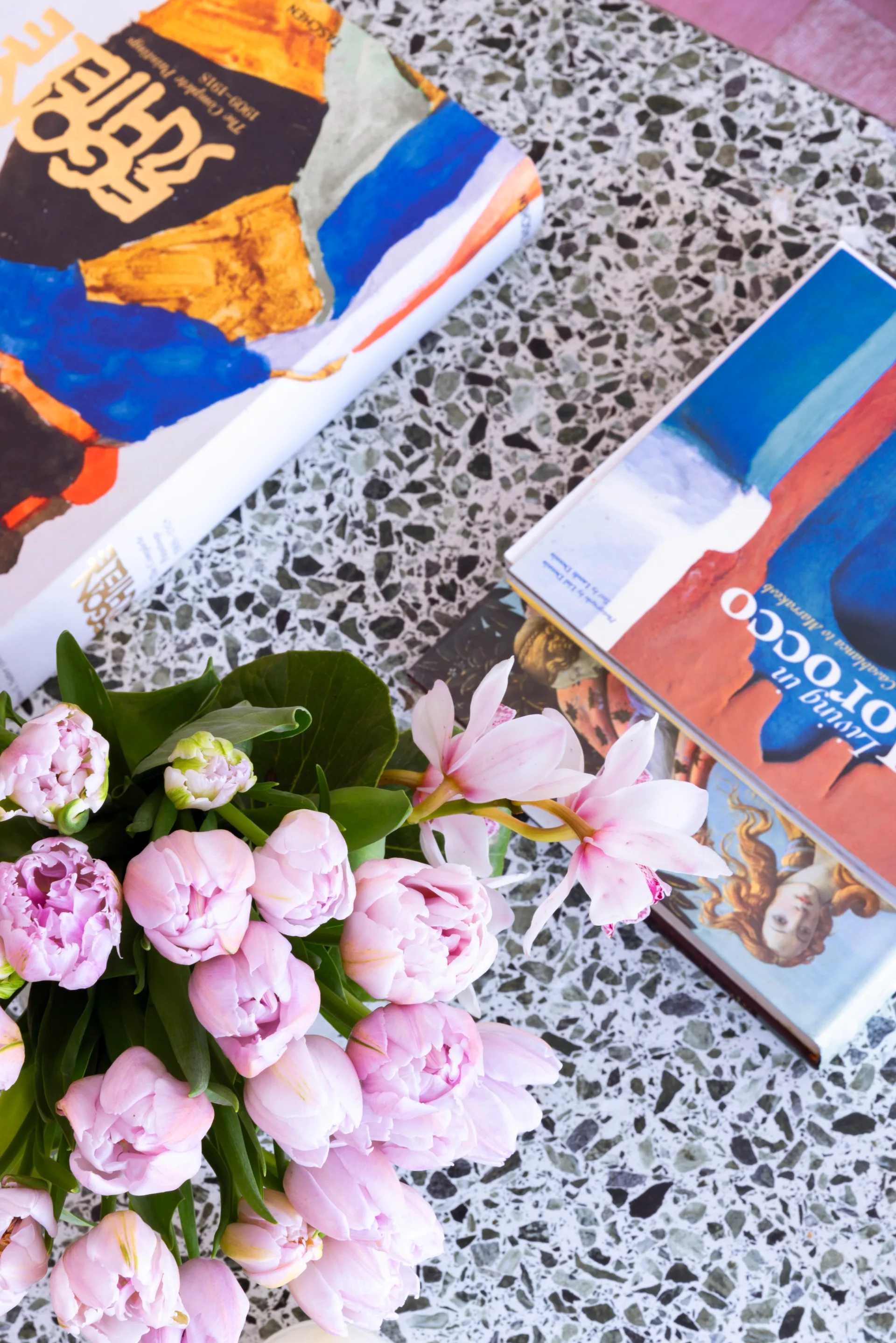 A vase of tulips on a terrazzo coffee table beside art books