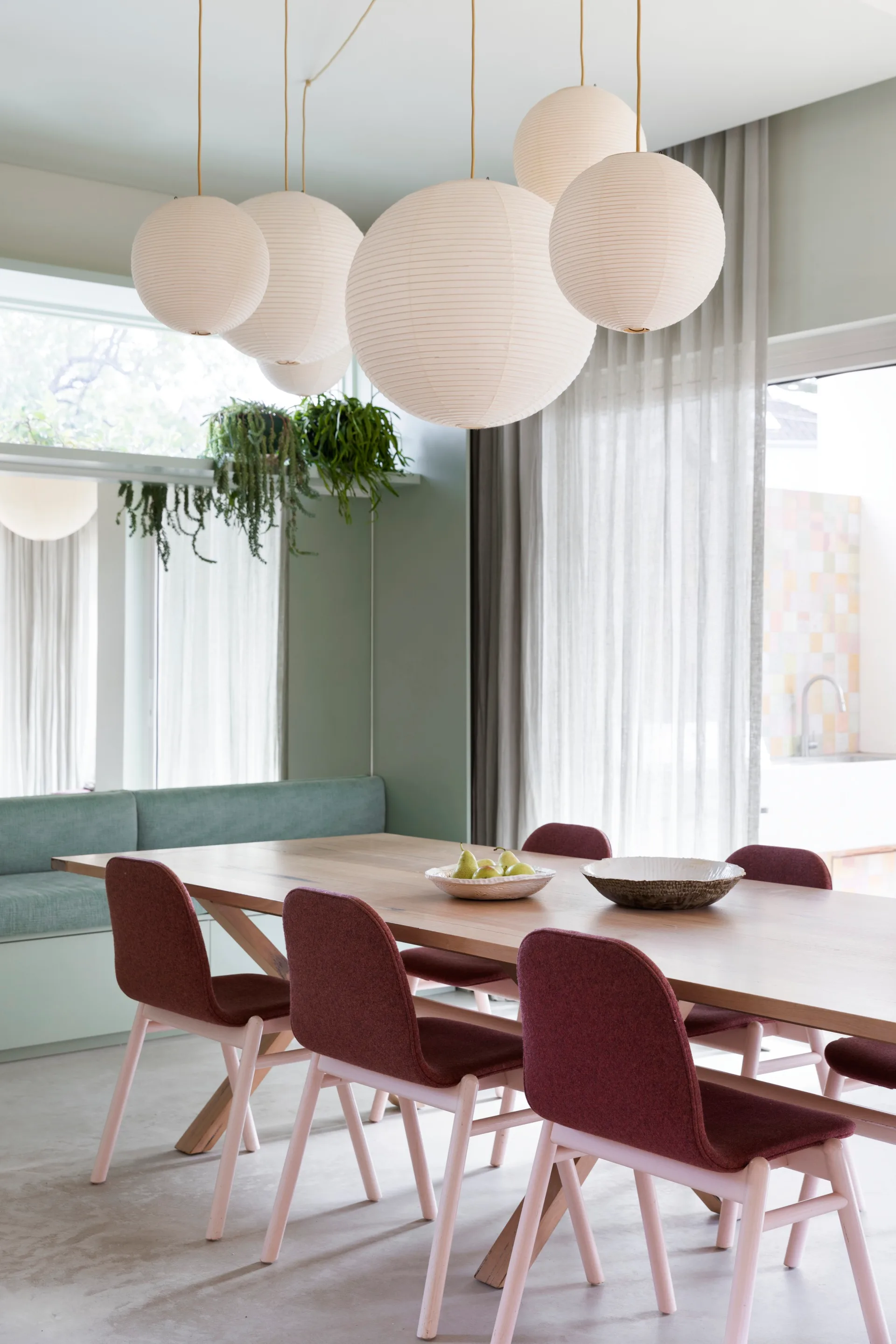 A contemporary dining room with pink and burgundy dining chairs and multiple paper lantern pendants