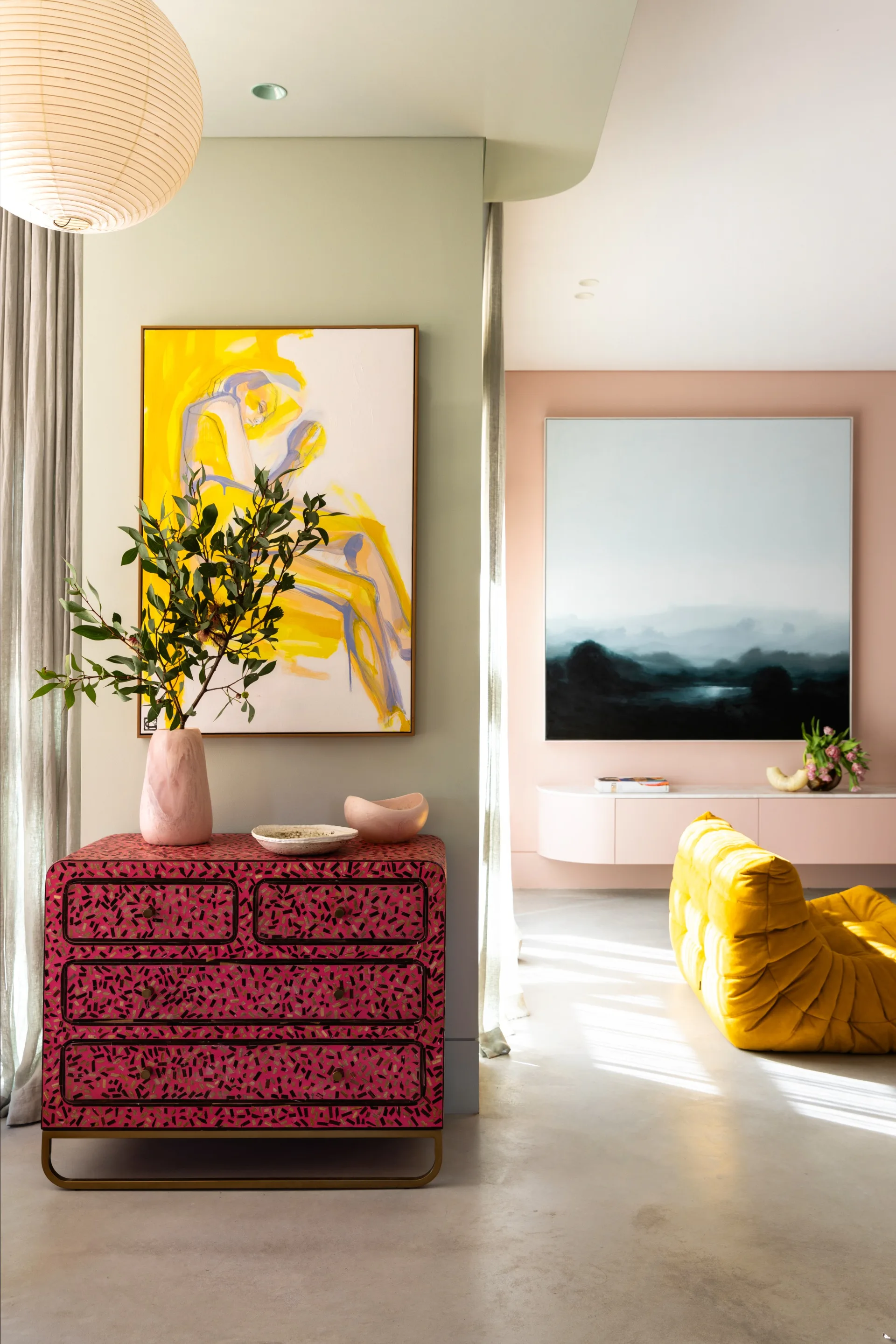 A lounge space with a mustard Togo sofa and a pink buffet cabinet