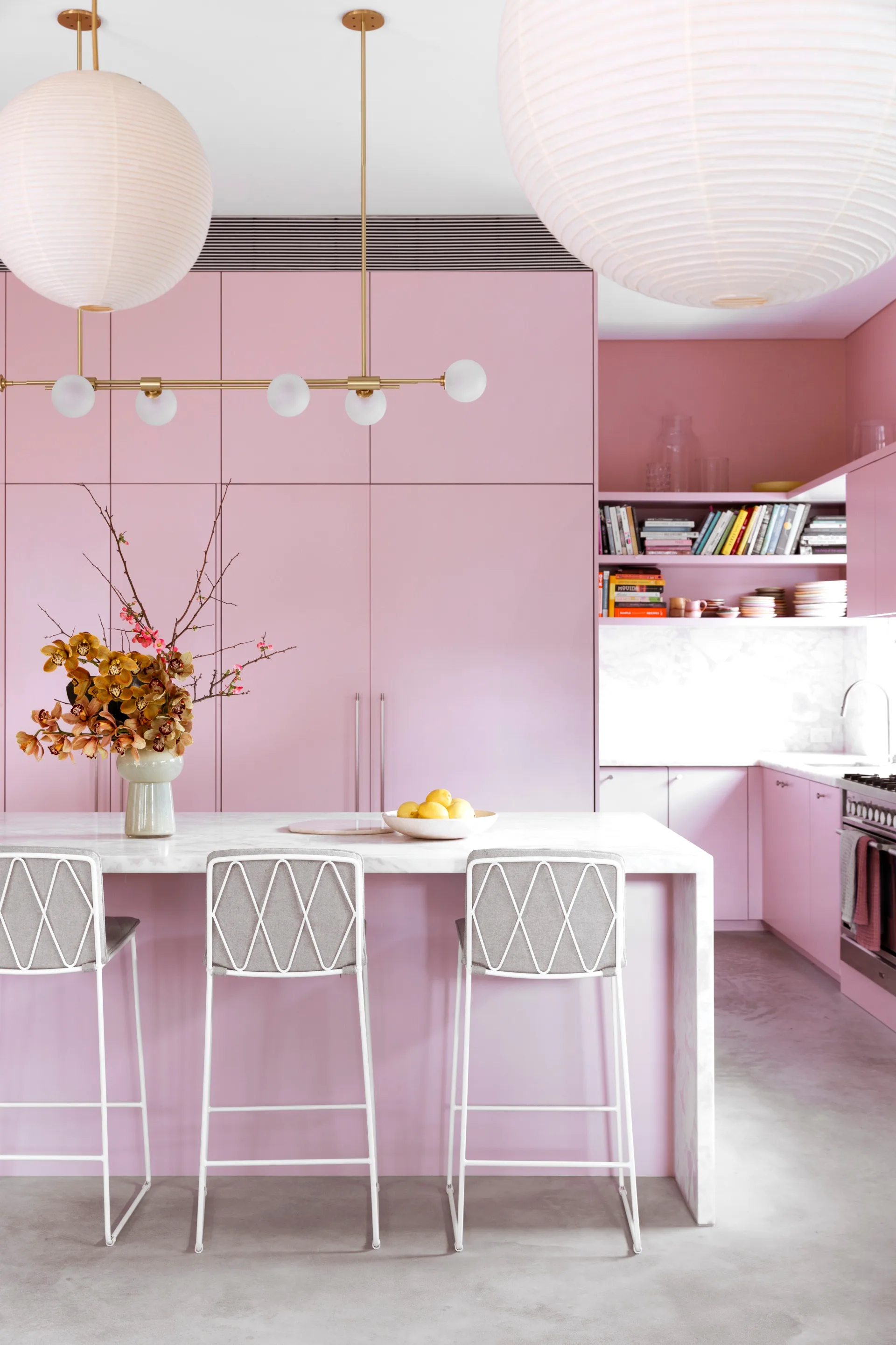 A pink kitchen with round lantern pendant lights and white barstools