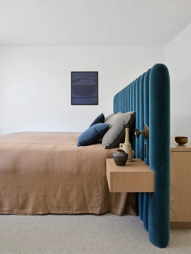 A contemporary bedroom with a custom blue velvet bedhead/partition and brown linen bedding