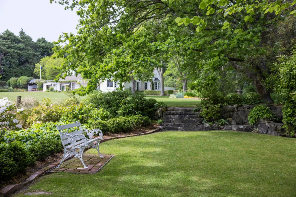 A green lawn space with an old ornate bench, a white homestead in the background