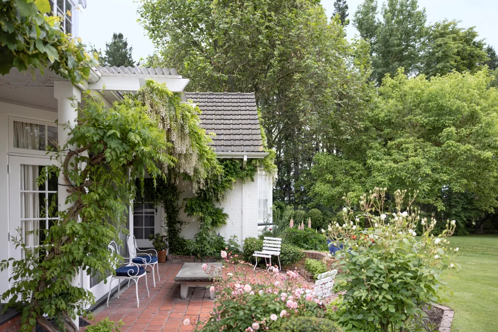 A wisteria-covered white homestead surrounded by trees and flowers in New Zealand