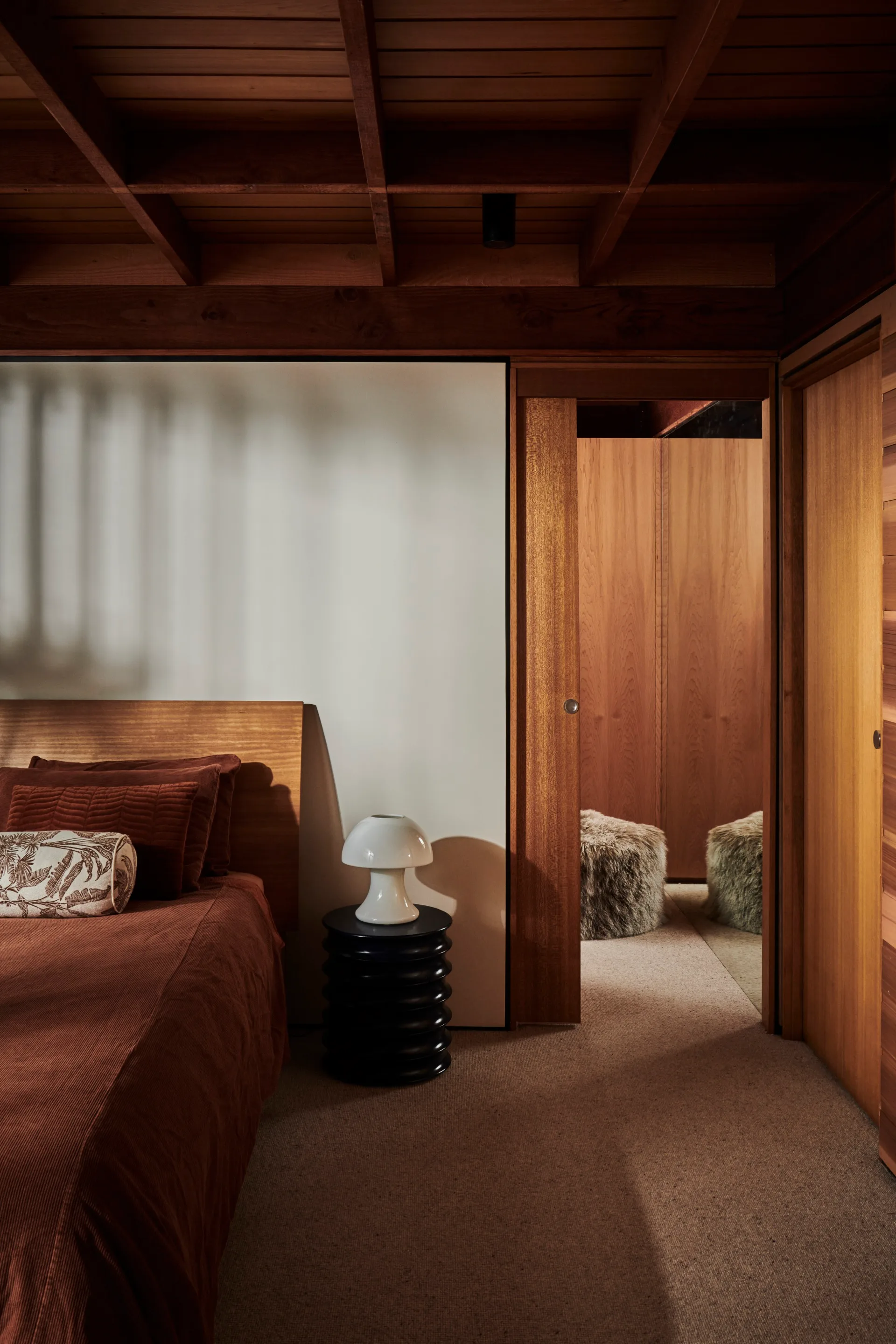 A timber-clad bedroom with a white mushroom lamp on a bedside table
