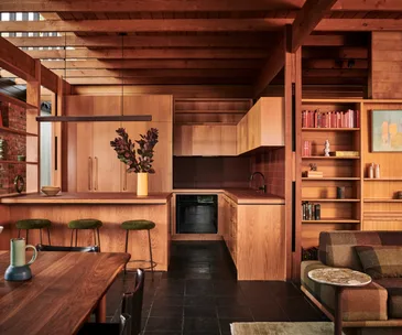 A timber-clad kitchen and living area with a plaid couch and green bar stools