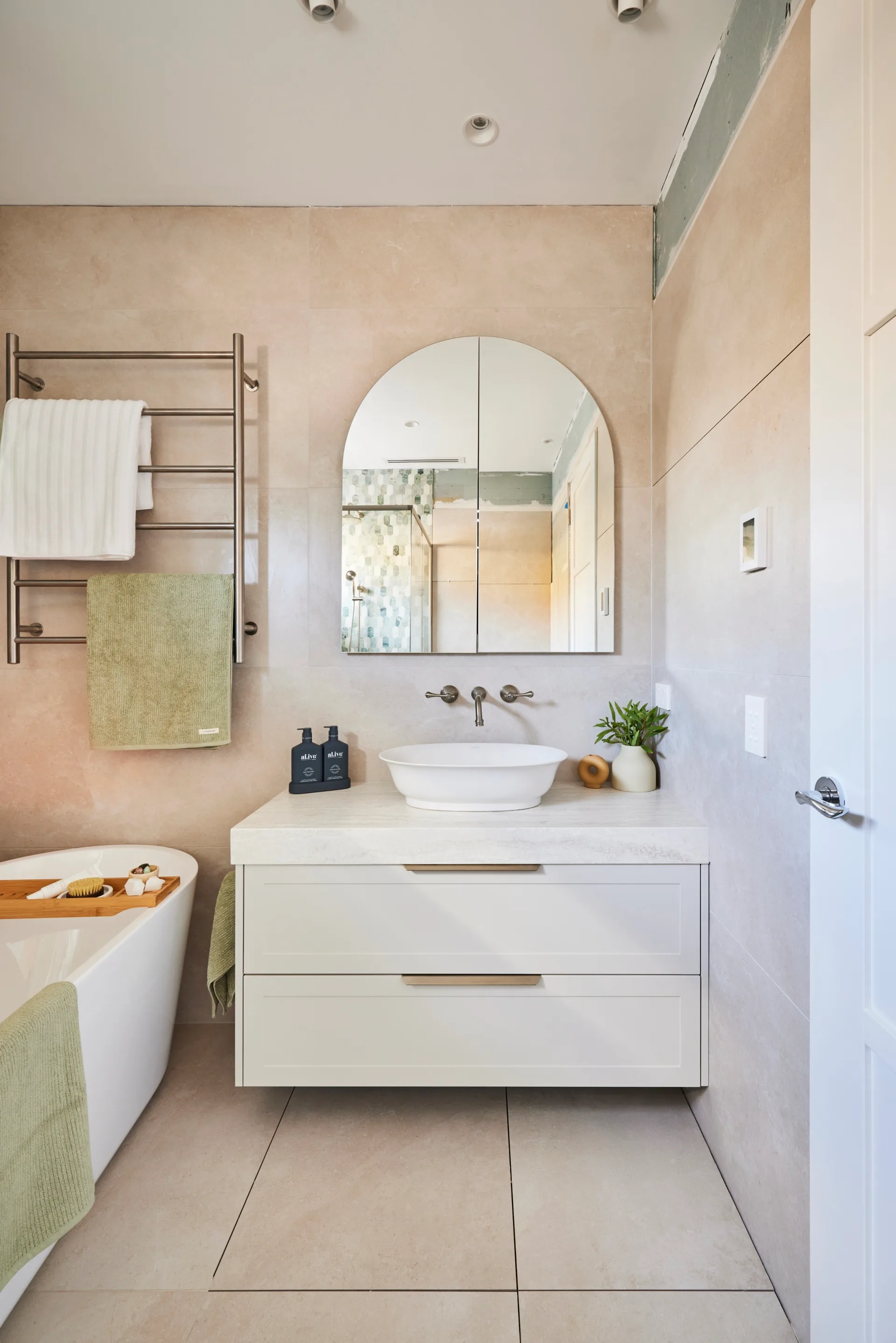 the block 2024 jesse and paige main bathroom with neutral tiles with white vanity and arched mirror