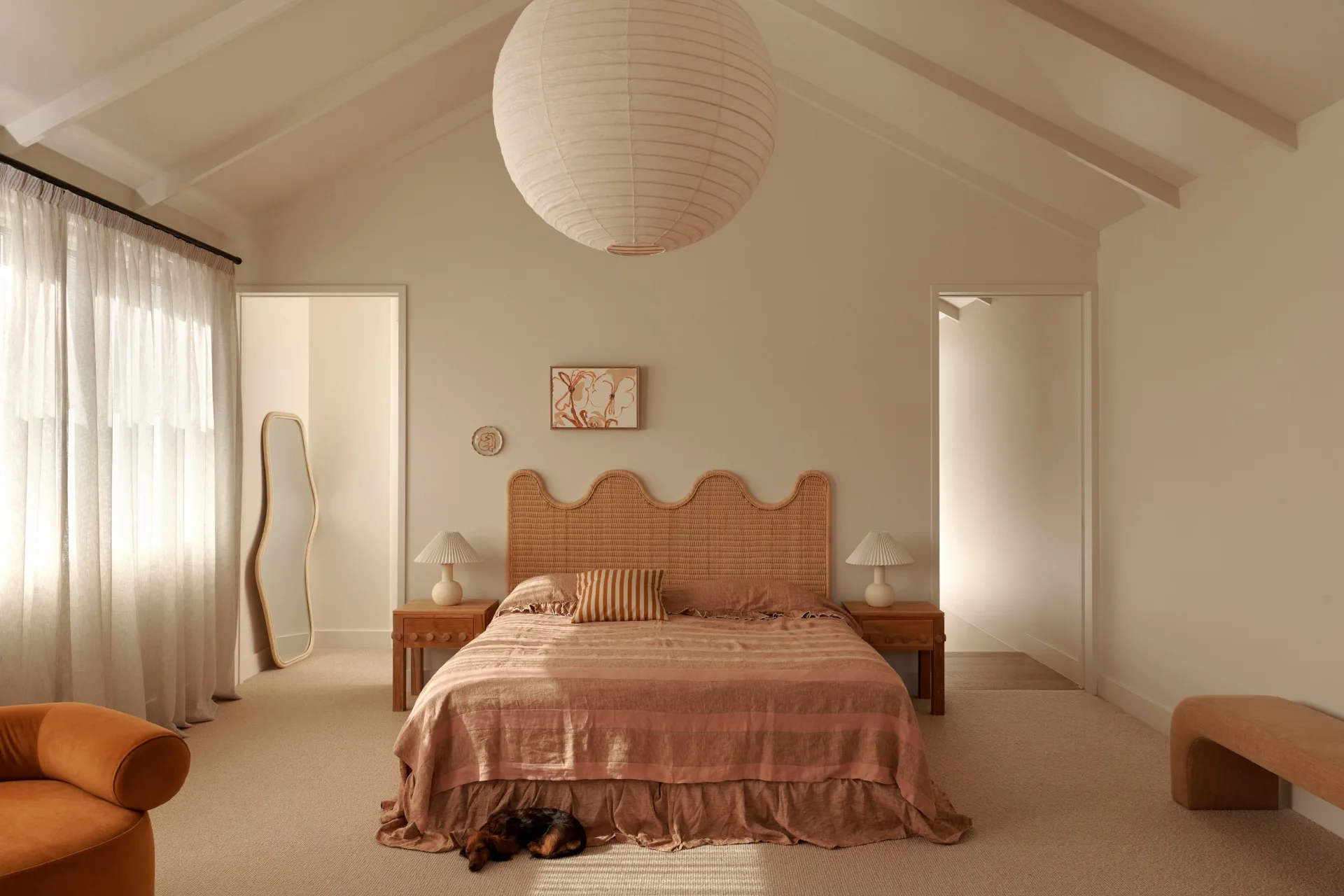 A large master bedroom with a rattan headboard and large paper lantern light