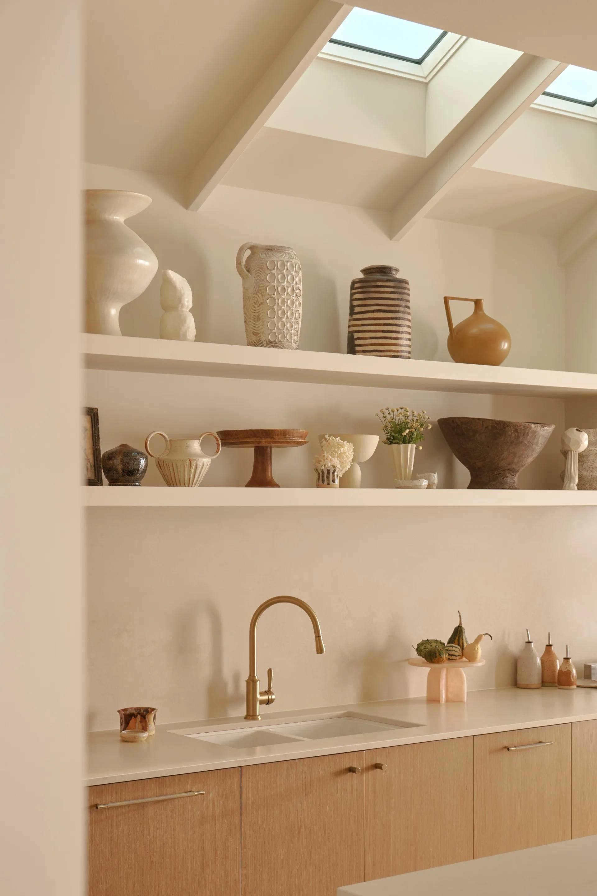 A neutral toned kitchen with floating shelves decorated with ceramics