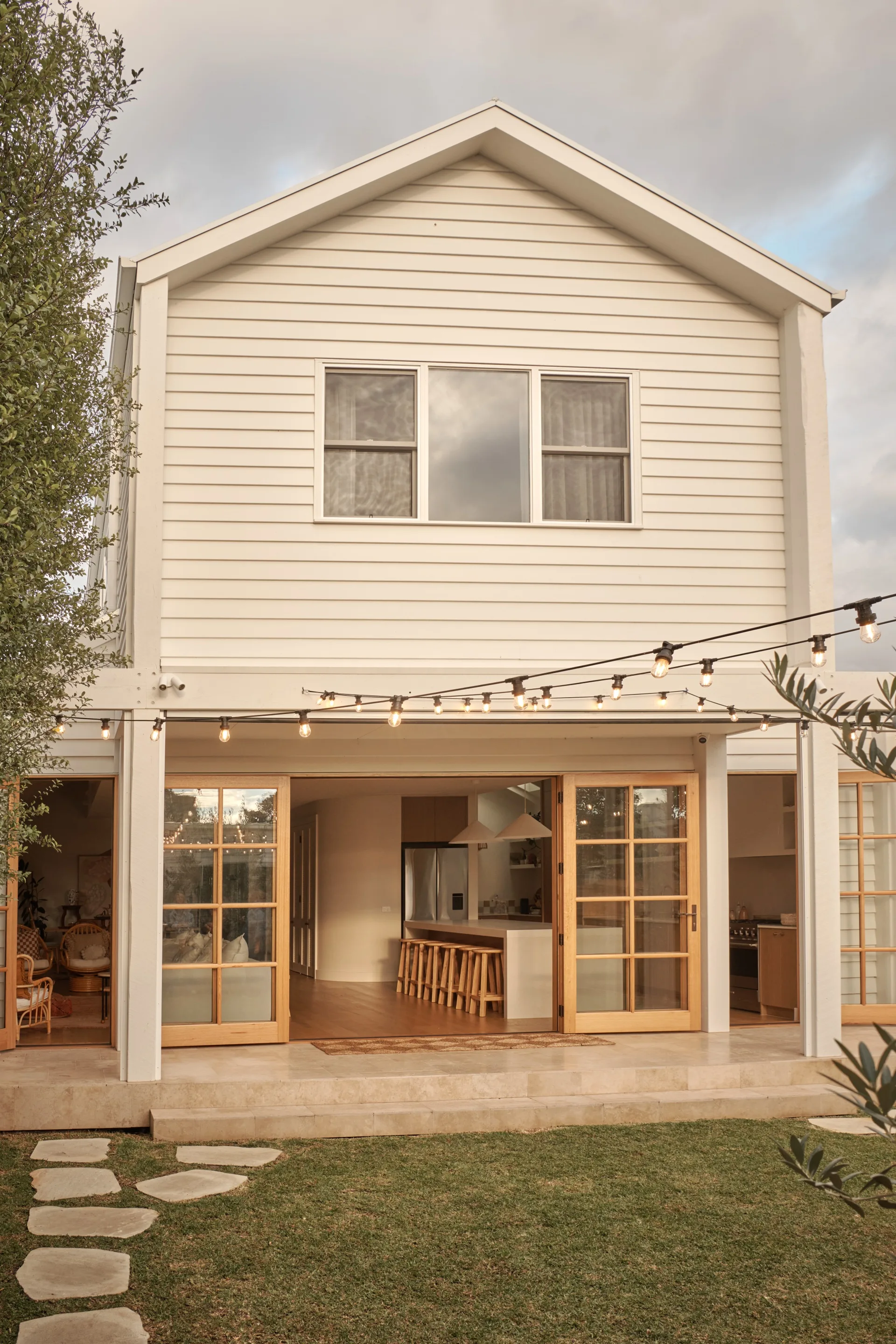 A weatherboard home with string lights above a lawn area