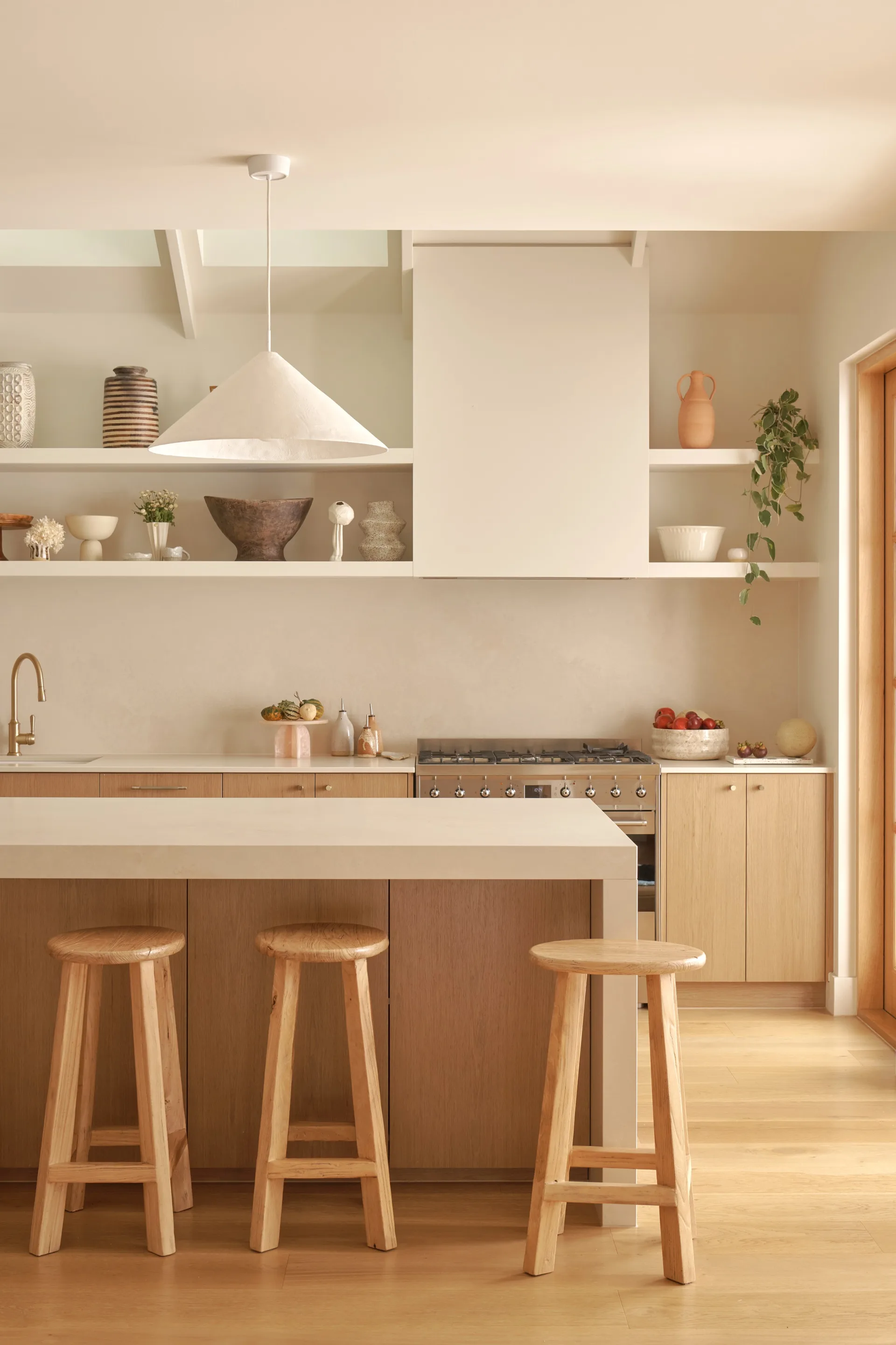A neutral tone kitchen with an angular island bench and white pendant light