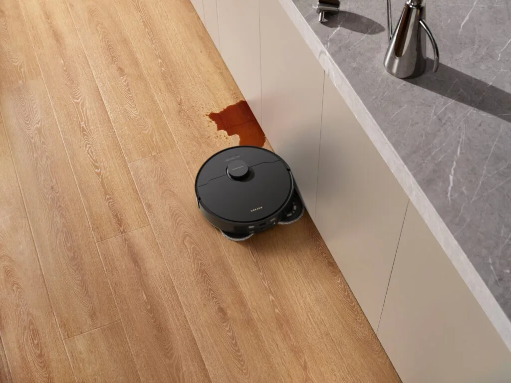 A robot vacuum cleaning a spill in a modern kitchen with timber floors.