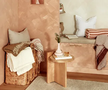 corner of room with reading nook, pillows, a basket, a side table and decorative objects with a warm ambiance