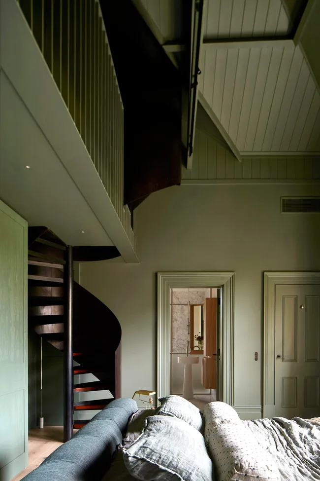 A green colour drenched broom with a spiral staircase and linen bedding