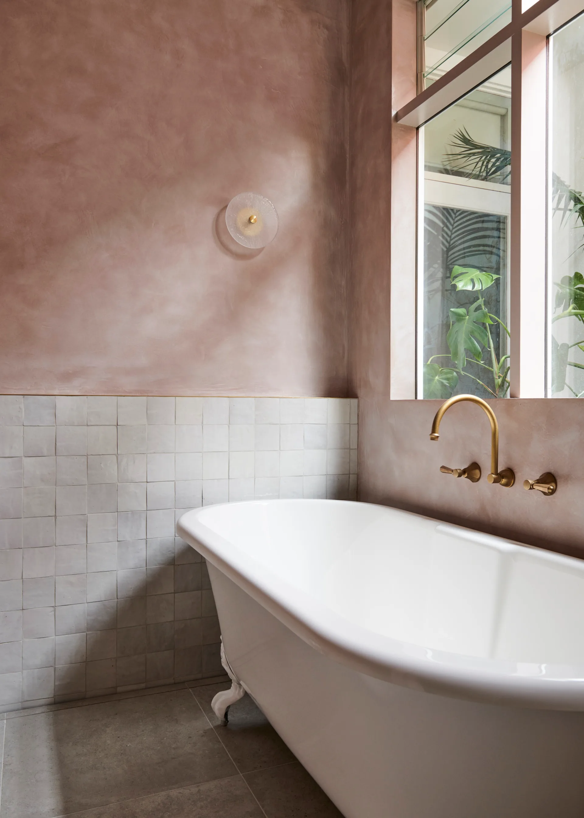 Pink microcement bathroom with a traditional clawfoot bath positioned against a window