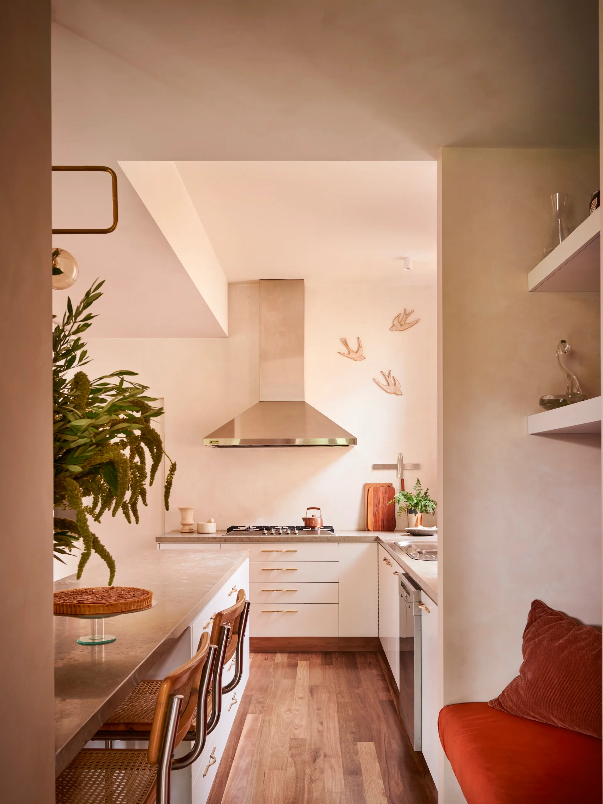 A warm white galley style kitchen with stainless steel rangehood and grey benchtops.