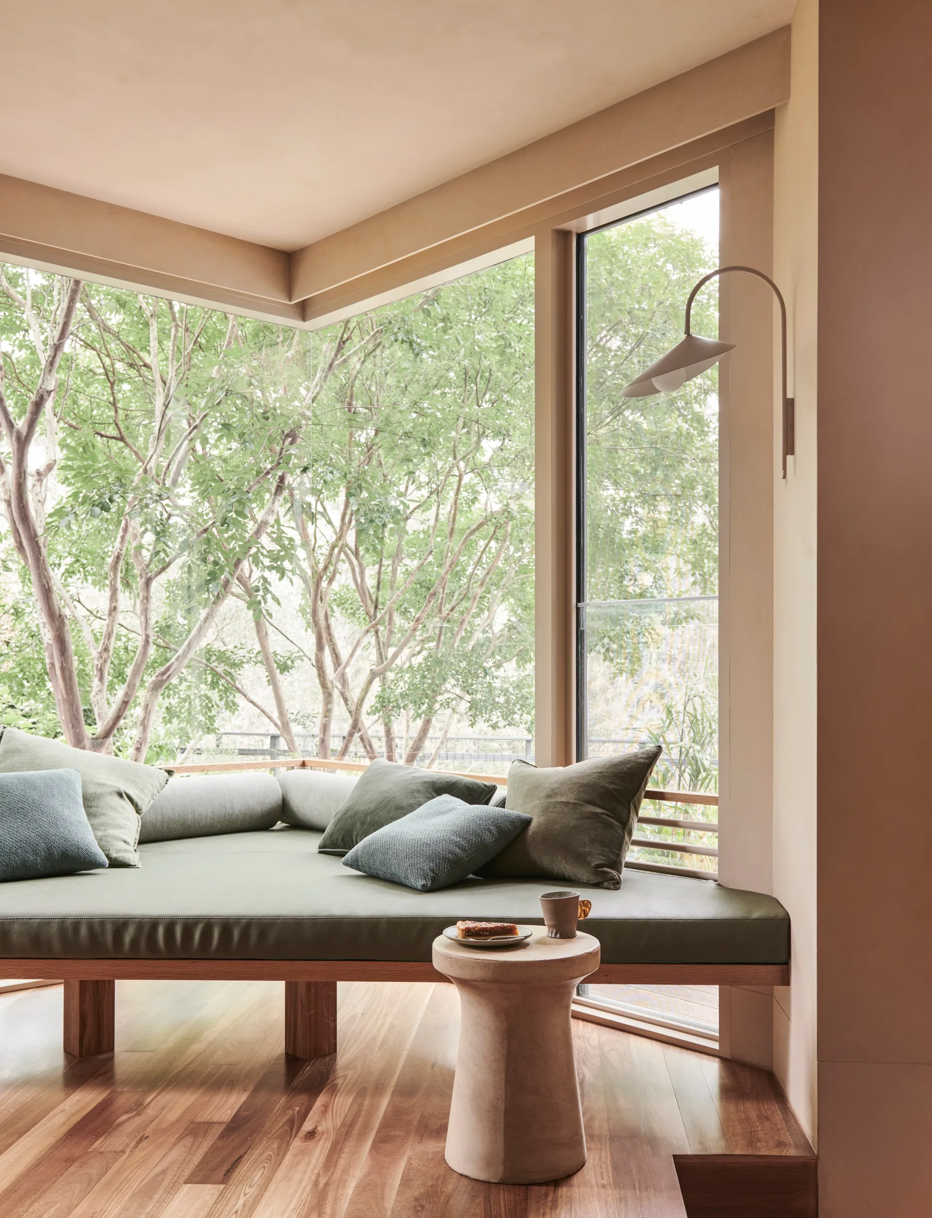 A window seat with green upholstery that looks out to trees.