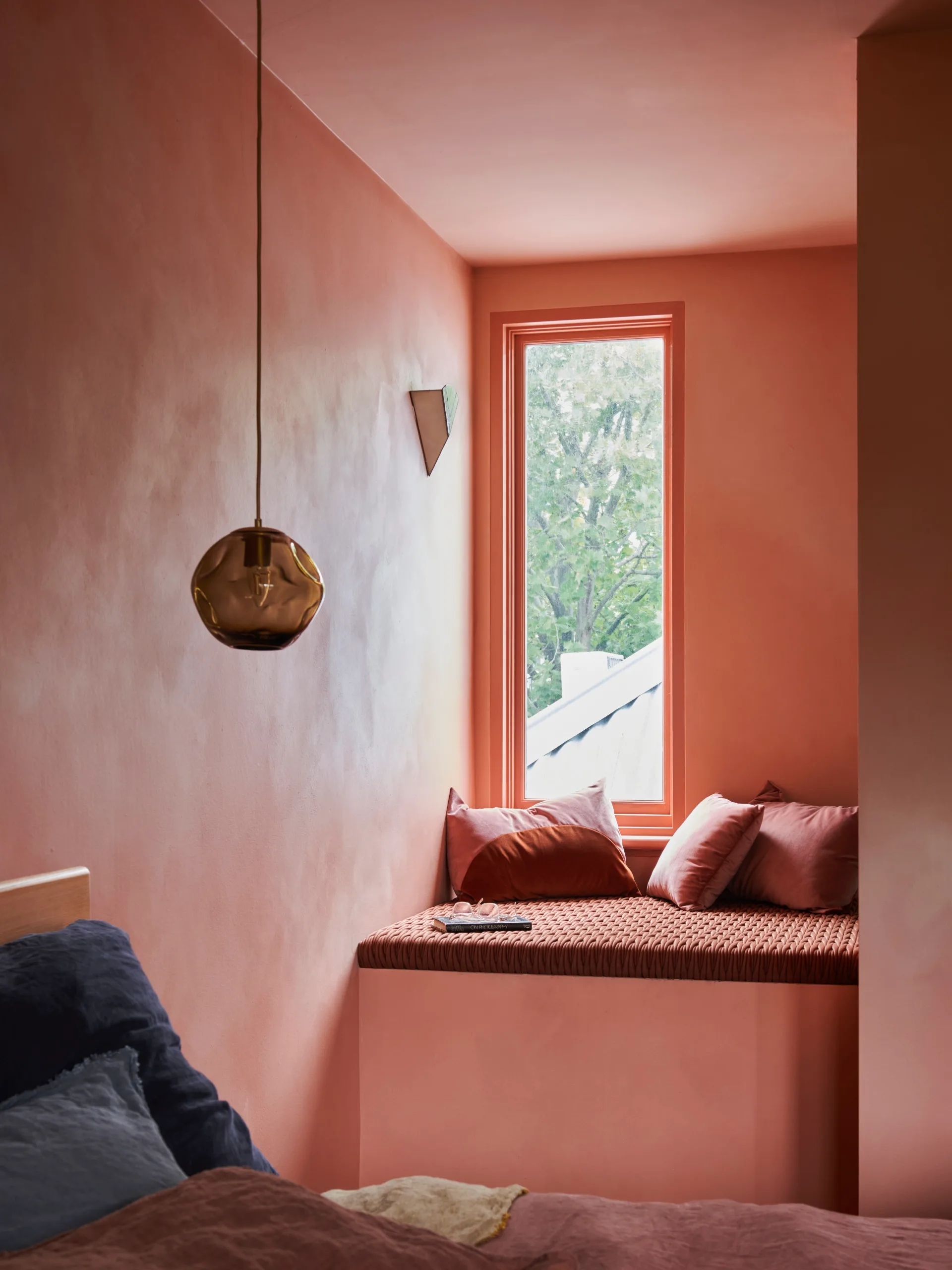 A small seating nook in a coral-coloured bedroom next to a vertical window