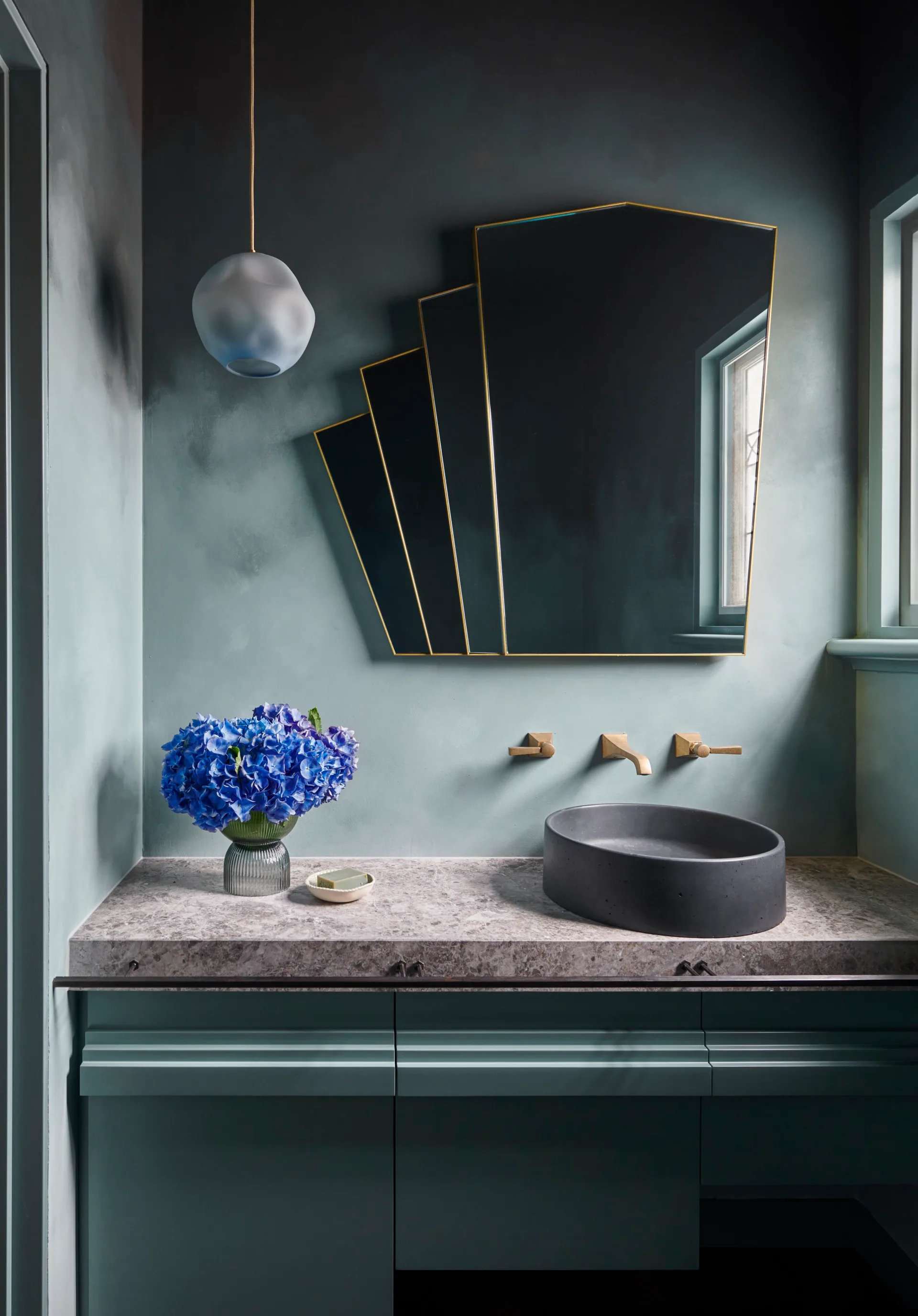 A teal-coloured microcement powder room with Art Deco mirror and limestone benchtop