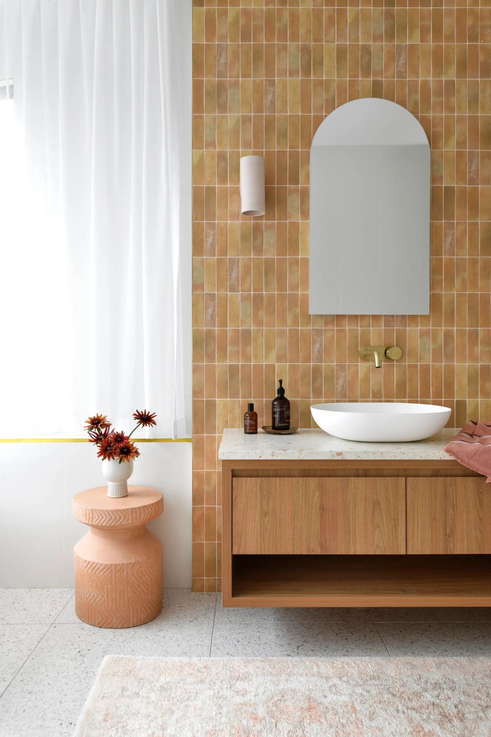 A bathroom with sandstone-coloured tiling and a floating timber vanity