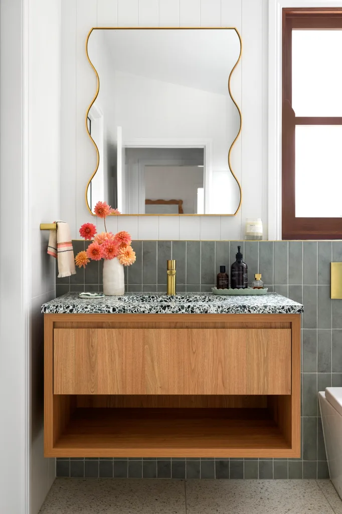 A bathroom vanity with a stone countertop and a wavy mirror hung above it