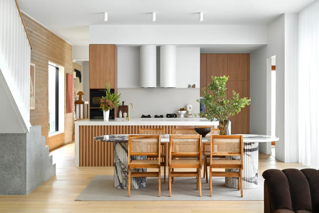 A neutral-toned open-plan living area with a marble dining table and timber-clad island bench