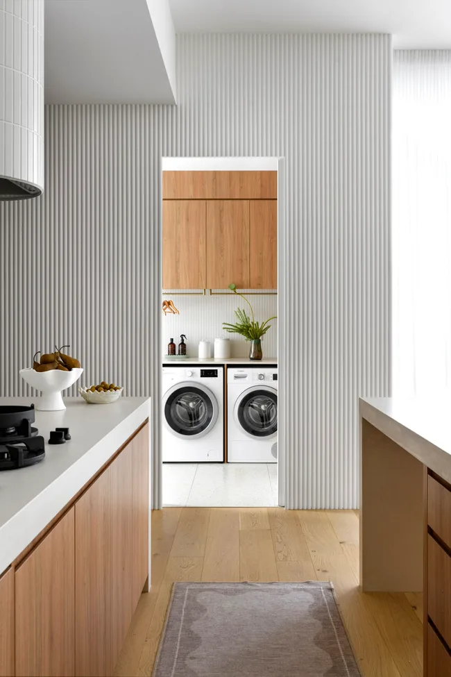 The view from the neutral-toned kitchen into the light-filled laundry with timber cabinetry