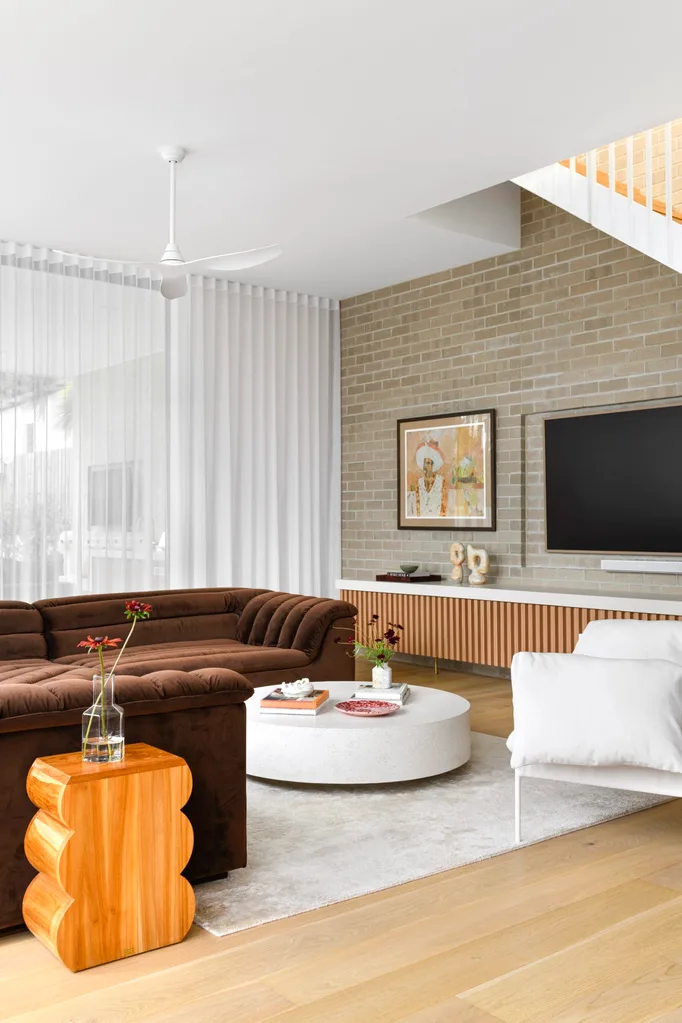 An open-plan living area with a brown vintage lounge and brick feature wall