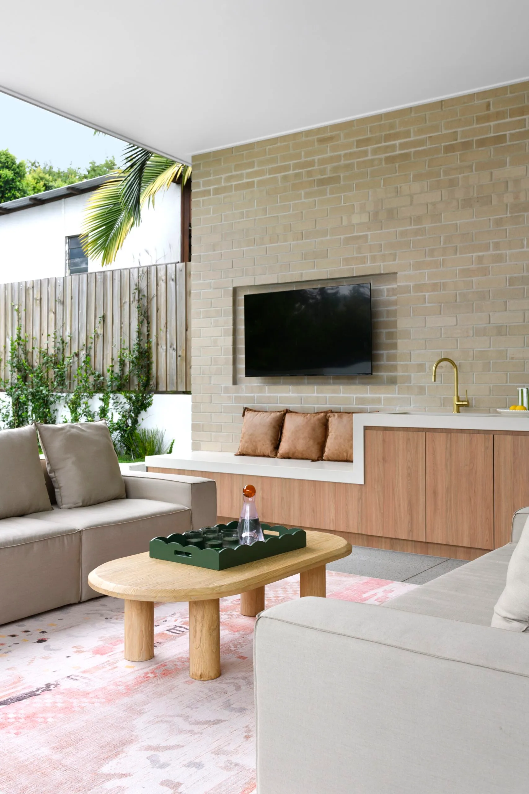An outdoor lounge area with a wall-mounted TV, grey lounges and a timber coffee table