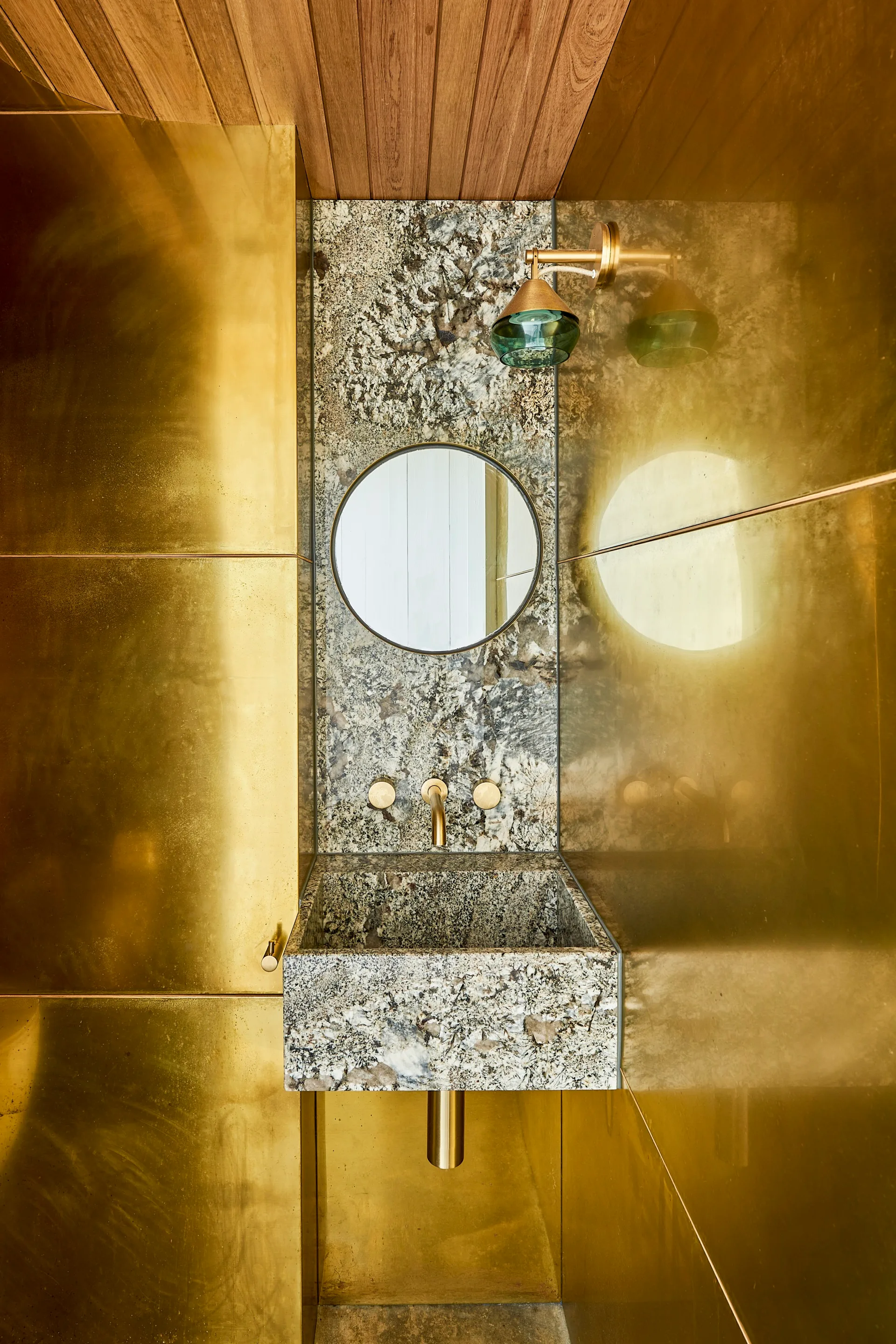 A gold metallic powder room with a marble sink and circle mirror