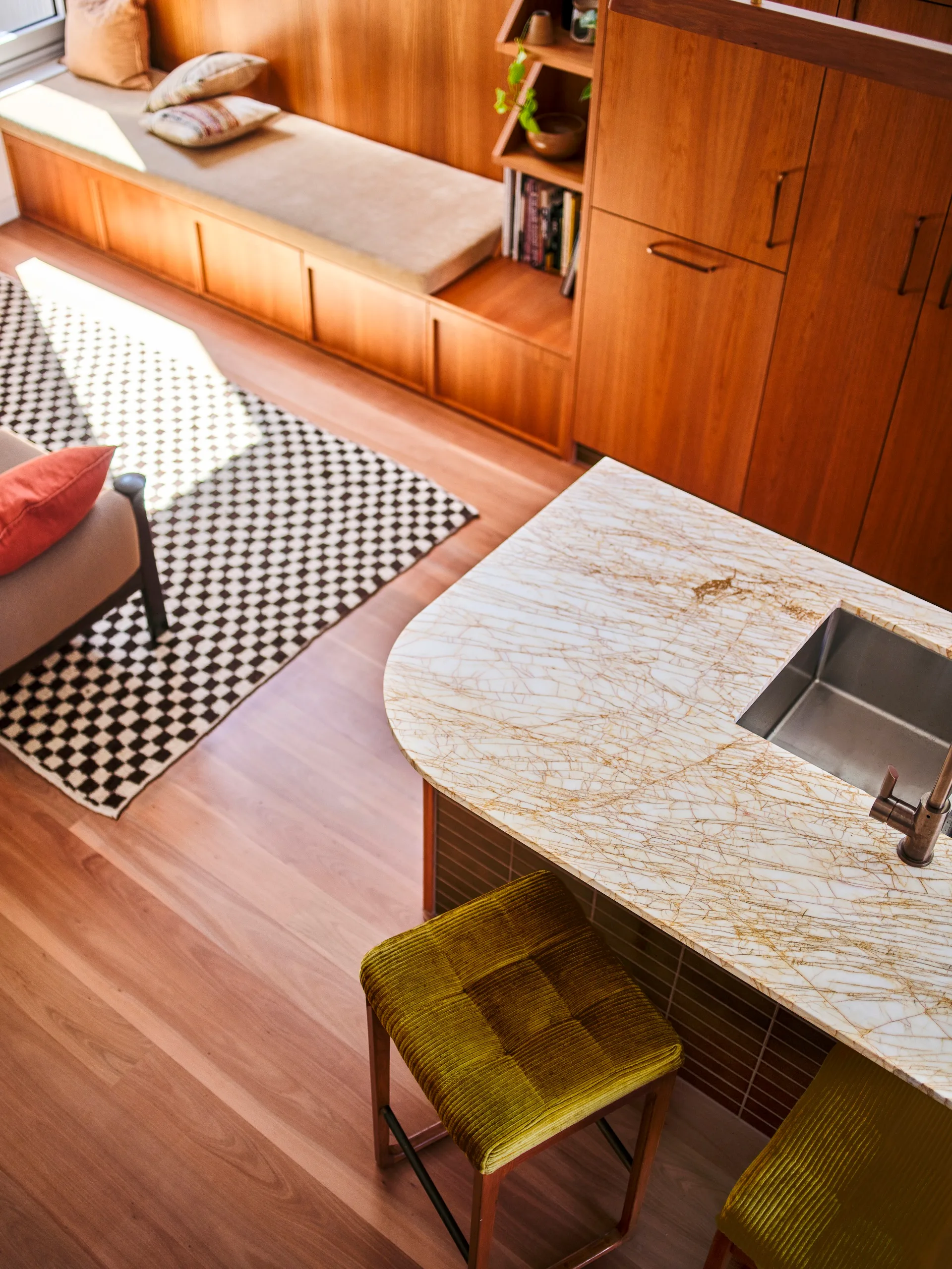 A striking stone benchtop in an open-plan kitchen and living area finished with timber cabinetry