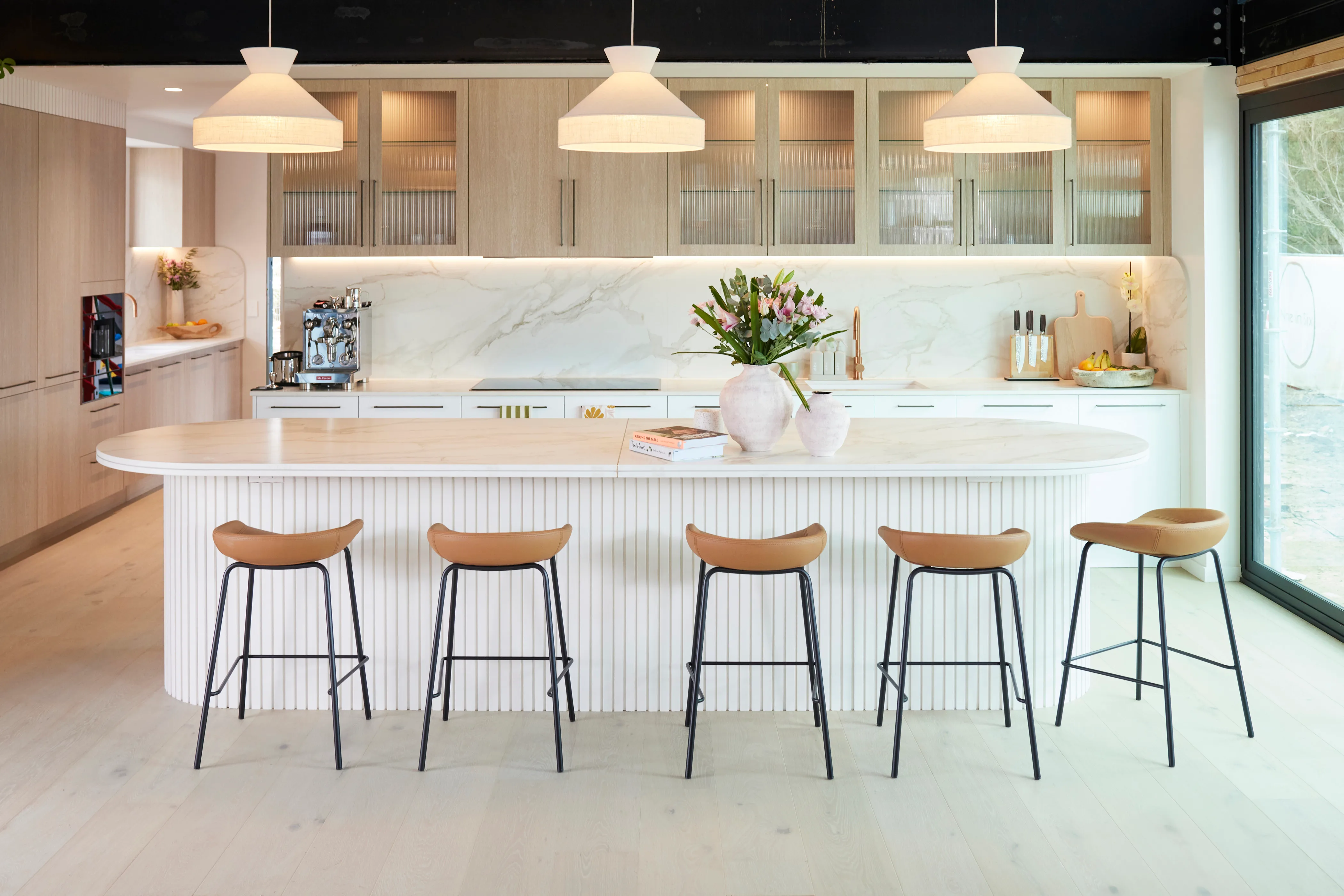 A white kitchen with a marble splashback and curved island bench