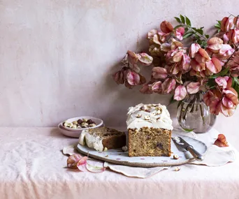 Spiced loaf with cream cheese icing sits on a pink tablecloth with pink flowers.