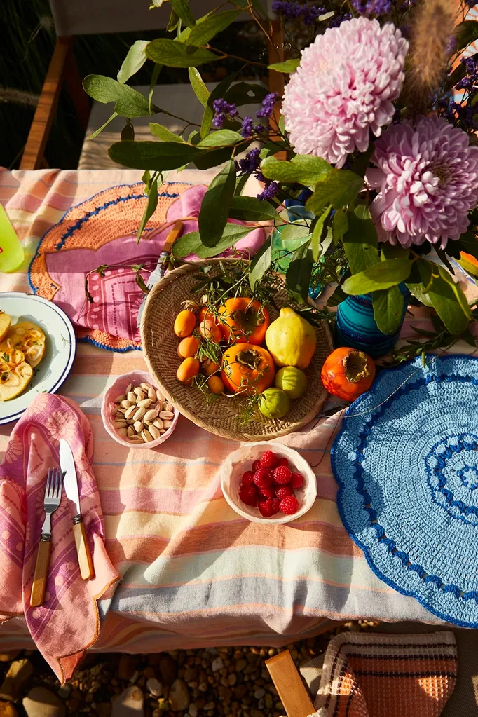 A dining table styled with a Sage x Clare tablecloth, flowers and a bowl of tomatoes