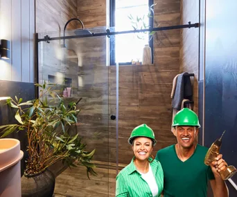 Andy and Deb positioned over Kylie and Brad's dark bathroom with wood-look tiles and a pink sink.