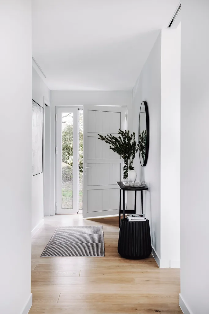 A white hallway with wooden floorboards and black furniture.